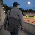 A man carrying the folded Full Game Chair over his shoulder on its strap, walking toward the stands