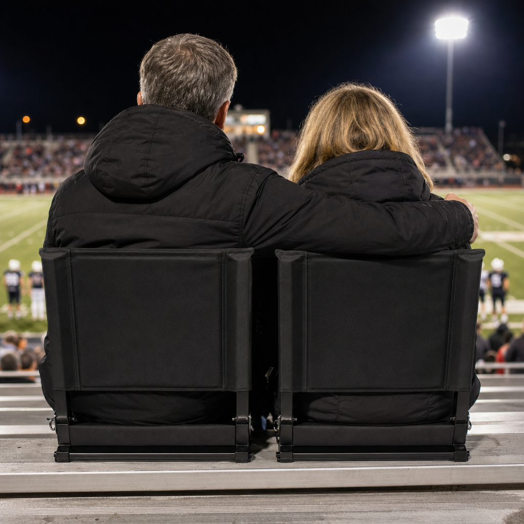 A couple seated in Full Game Chairs from behind, stadium floodlights over the field at night